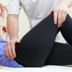 Male Osteopath Treating Female Patient With Hip Problem